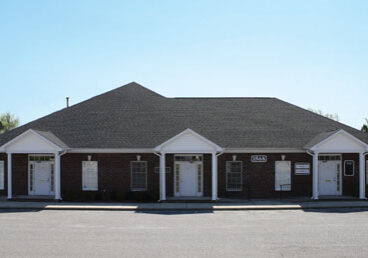 A symmetrical, single-story brick building with a dark roof under a clear sky.